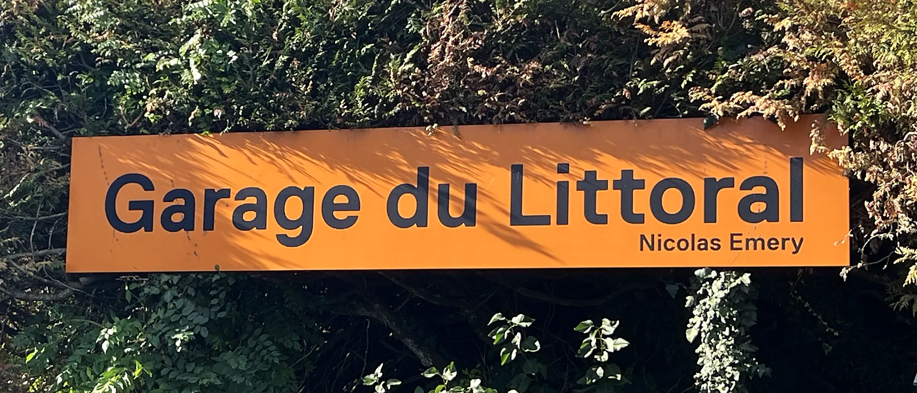 L'enseigne orange Garage du Littoral, Nicolas Emery, devant la haie